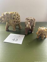 Three carved stone elephants of varying sizes displayed on a green surface with natural light, showing their carved hollow patterns and baby elephants inside.