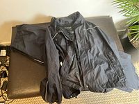 Photo of black Froggtoggs motorcycle rain gear including jacket and pants laid on a bench, showing overall look and fabric texture.