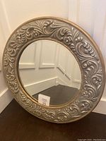 Front angled photo showing full mirror face and ornate frame design with embossed scroll and floral motifs.