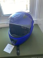 Front and side view of blue motorcycle helmet with clear visor, showing scratches on surface and attached chin strap.