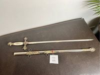 Silver-tone Knight’s Templar style decorative sword with detailed metal handle and crossguard, accompanied by matching metal scabbard with red cross emblems, displayed on a dark surface.