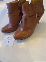 Photo showing front and side view of pair of brown ankle boots with zipper and buckle, highlighting the overall shape and color.