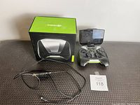 Photo showing Nvidia Shield gaming controller, controller holder box, charging cable, and lot number card on black textured surface