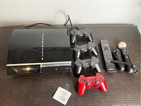 Overview photo of Sony PlayStation 3 console, four controllers (three black and one red), PlayStation Move controllers, and remote control arranged on surface