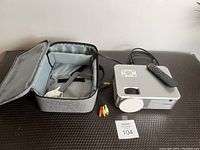 Projector with remote and AV cable next to carrying case on black surface