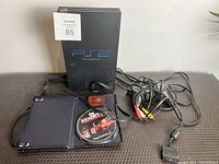 Sony PlayStation 2 console standing vertically with power and AV cables attached, Def Jam Vendetta game disc shown inside an open case.