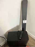 Sound bar leaning against wall next to subwoofer with remote on top of subwoofer