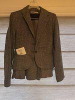 Gray and white herringbone tweed blazer with matching pleated skirt hanging on a hanger.