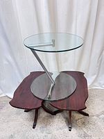 Front view of glass-top accent table on top of two wooden tables with carved edges and pedestal bases, showing overall design and material contrast.