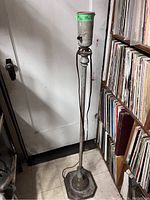 Full view of antique metal floor lamp standing next to a bookshelf and a door. Shows the tall, narrow pole and socket at top.