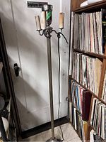 Full view of the antique floor lamp standing next to a bookshelf and door, showing the dual candle-style light fixtures and metal stem.