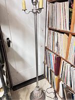 Full view of tall antique floor lamp standing on floor near door and shelves of records.