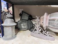 Six assorted sconce lamps grouped on shelving, showing different designs and metal finishes with glass panels, some with scrollwork mounts.