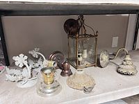 Photo showing seven assorted vintage wall sconces on a shelf, various materials and designs visible.