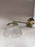 Wall-mounted extendable pendant lamp with brass arm and frosted glass shade featuring starburst pattern.