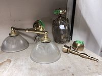 Photo showing 3 brass lighting fixtures: two wall sconces with pleated frosted glass shades and one pendant light with glass enclosure and brass handle