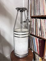 Chrome pendant cylinder lamp with frosted etched glass shade on wood table beside bookshelf