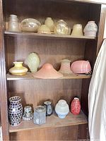 Photograph of multiple colored glass lamp shades on wooden shelves showing different shapes and textures including domed and flared.