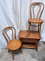 Three vintage wooden chairs with rounded backs, two on the floor and one placed on top of a wooden drop-leaf side table with a lower shelf.