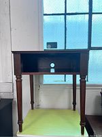 Small vintage wooden writing desk shown from front with open shelf containing cable hole and turned legs