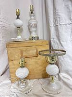 Four vintage table lamps arranged around a wooden box, showing details of milk glass hobnail pattern and ceramic lamp with painted floral motif.