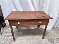 Front view of vintage wooden accent table showing rectangular top with wear and single drawer with white knobs.