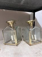 Two brass and glass ceiling pendant lights on a shelf showing front and side views. Each has square glass panels with an etched star pattern and brass mounts with wiring for electric bulbs.