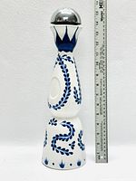 Full view of the tall white ceramic bottle with blue painted designs and ruler for scale, showing the shape and decorative pattern.