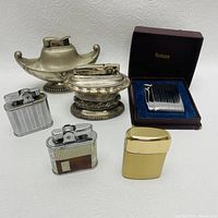 Group photo of 6 Ronson lighters showing two ornate table lighters, three pocket lighters, and one boxed lighter.