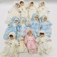 Top down view of 13 small porcelain baby dolls arranged in three rows, showing full outfits and faces.