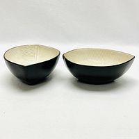 Two decorative bowls, one upright and one inverted, showing cream interior with leaf vein lines and matte black exterior.
