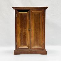Front view of wooden doll-sized wardrobe with closed doors, showing wood grain and panel details.