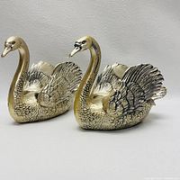Front angle view of two cast metal swan figurines with detailed feathers and a gold-silver finish.