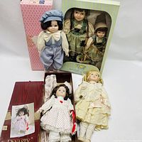 Four porcelain dolls displayed with two original doll boxes, one pink and one red with Dynasty Doll Collection label.