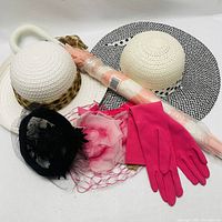 Photo showing three women’s pretend play hats, bright pink gloves, and an umbrella still in its packaging on a white background.