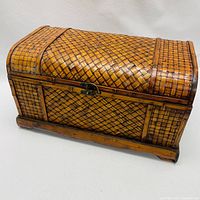 Front and side view of a small woven trunk showing curved lid, metal latch and wood frame