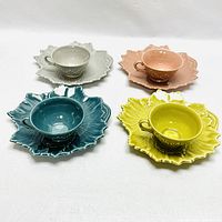 Four Woodfield ceramic cups on matching leaf-shaped ceramic plates in beige, pink, teal, and yellow colors arranged on a white background.