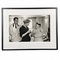 Framed black and white photograph showing two women and one man in a social setting, holding glasses.