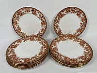 Stacked sets of 14 round serving plates with brown floral and gold patterns on white bone china.