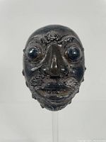 Front view of embossed silvered metal mask on lucite stand