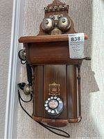 Front view of wooden wall telephone showing twin bells, rotary dial, handset and crest decal