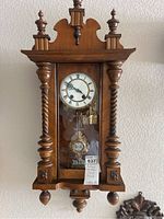 Front view of antique German wall clock with visible Roman numeral face, pendulum, and ornate wooden details on case.