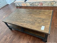 Coffee table showing wood grain top, black metal frame, caster wheels and lower shelf.