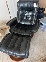 Front view of black leather recliner and ottoman showing tufted upholstery and wood base