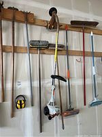 Full view of all cleaning and yard tools hanging on garage wall, including the Stihl weed eater, push brooms, mop, and dustpan.