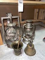 Four decorative antique items: two metal lanterns, brass mortar and pestle, and brass bell.