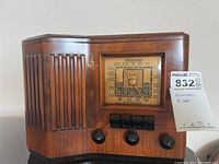Front view of Emerson antique radio showing wooden casing, tuning dial, control knobs, and tag with lot information.
