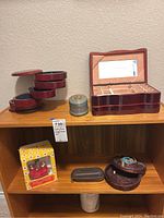 Wooden tiered rotating jewelry box and hinged lid jewelry box with mirror shown on wooden shelf, vintage music box and storage basket below, Timberland glasses holder also visible