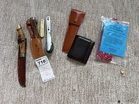 Lot showing two fixed blade knives with sheaths, folding camping spoon with leather case, black leather wallet, and Kool Kollar cooling bandana sealed in plastic.