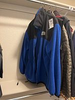 Blue and black fleece jacket by The North Face hanging on a rack
